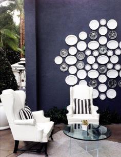 Patio with dark blue walls, white wing chairs and an arrangement of plates on the wall.