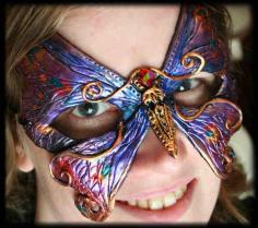 
                    
                        PURPLE AND GOLD BUTTERFLY MASK This swallowtail butterfly mask is iridescent purple, blue and gold highlights. A red gem with rainbow sheen forms the butterfly's head. This mask is entirely hand sculpted and hand painted with an artist's stamp at the back. Roughly 6" wide by 5.5" tall. - Unique Personalized Masks by Namingway | Art and Design
                    
                